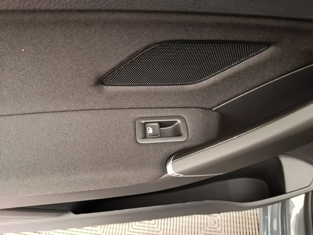 Gros plan sur la poignée intérieure et le bouton de verrouillage de la porte côté conducteur d’un Volkswagen Touran gris clair.