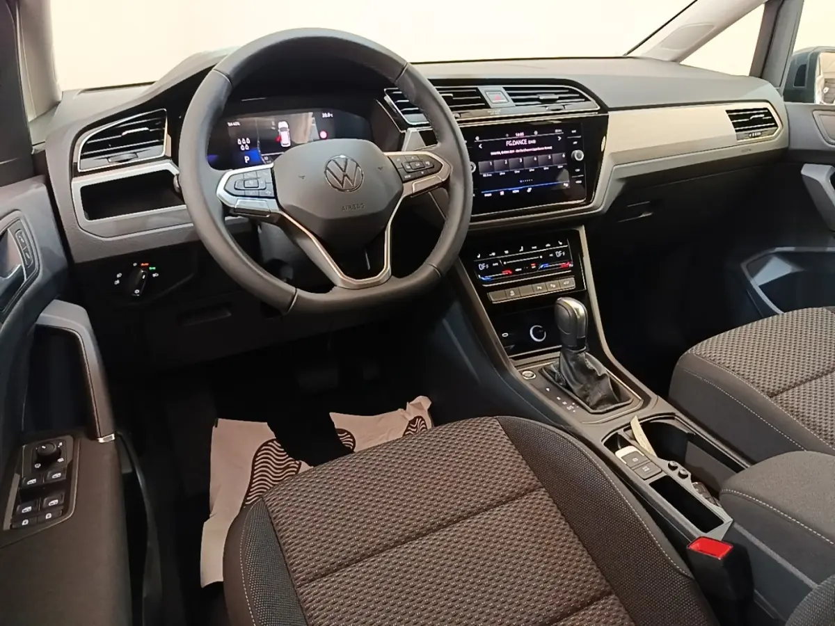 Vue intérieure côté conducteur du Volkswagen Touran 2024, tableau de bord noir avec écran tactile central et volant multifonctions.