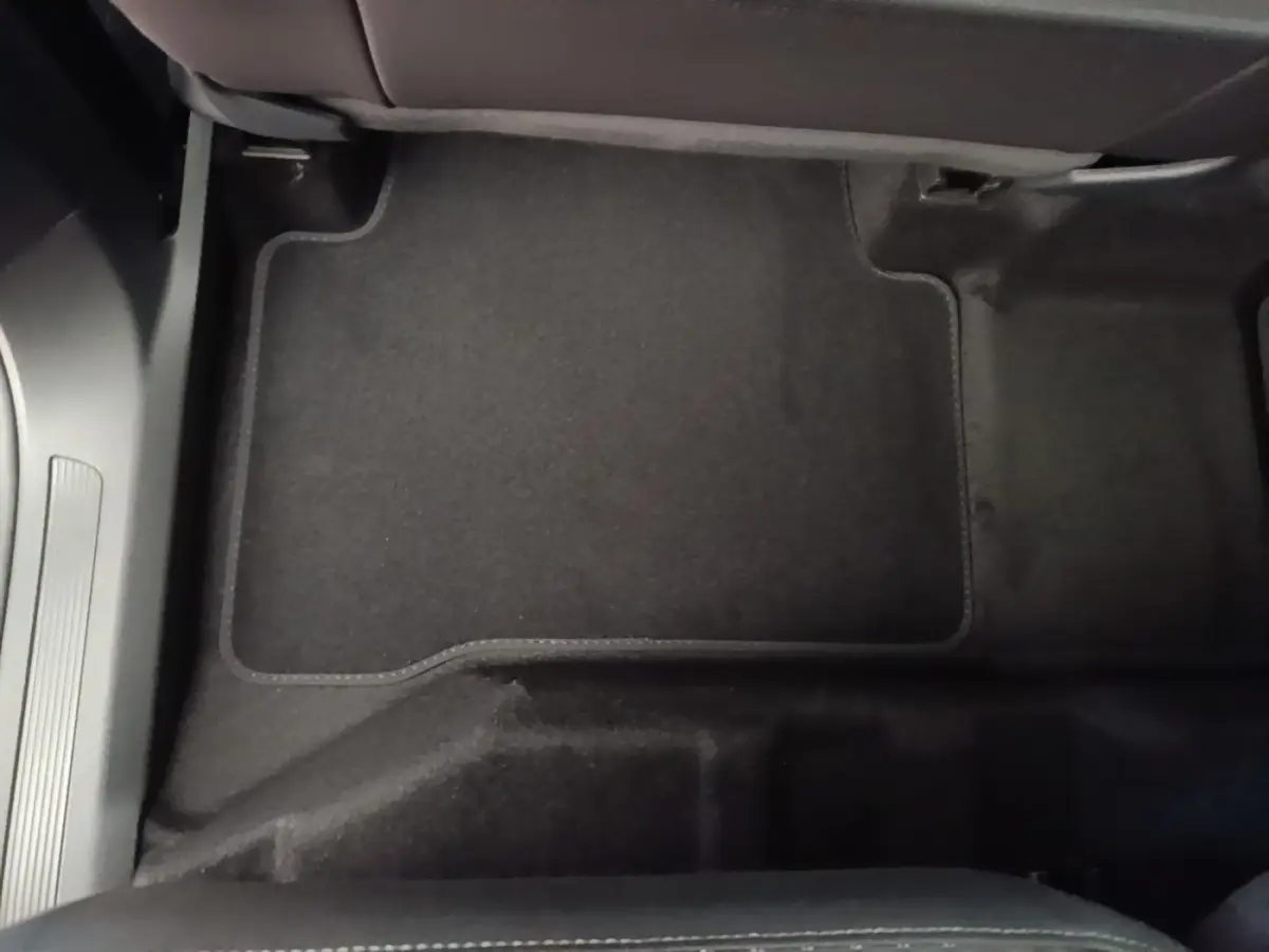 Vue rapprochée du tapis de sol noir côté passager avant du Volkswagen Touran 2024 gris clair.