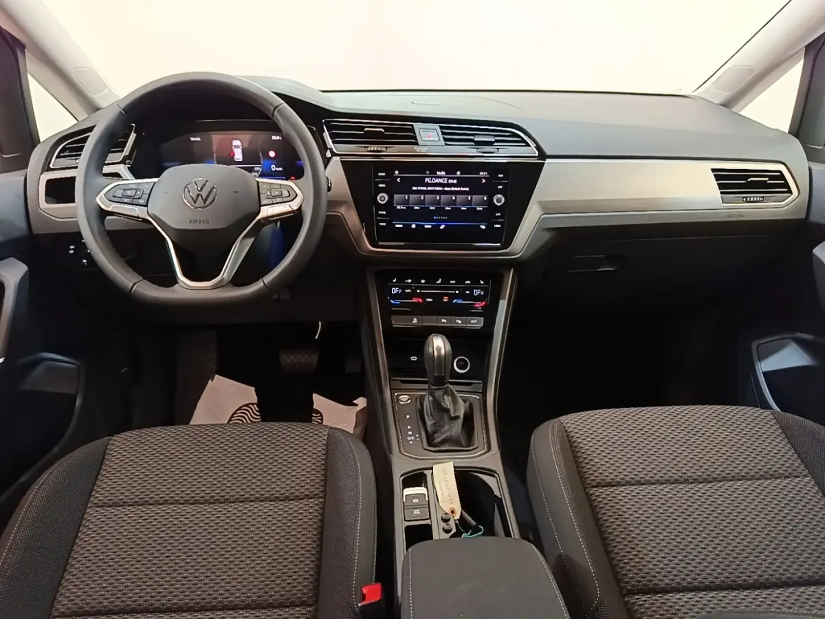 Vue intérieure avant du Volkswagen Touran 2024, tableau de bord gris clair avec écran tactile et volant multifonctions cuir.