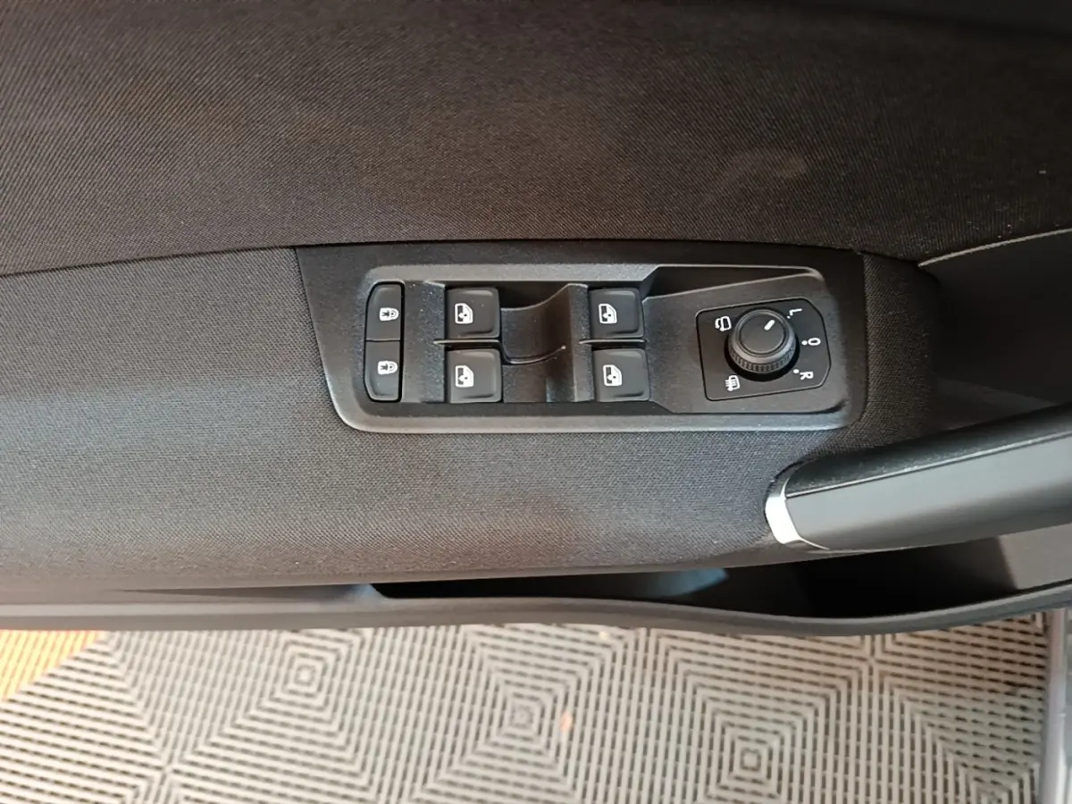 Gros plan sur la commande des vitres et rétroviseurs côté conducteur d’un Volkswagen Touran gris clair 2024.