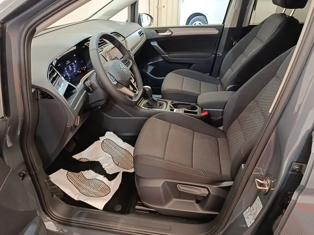 Vue intérieure côté conducteur du Volkswagen Touran gris clair 2024, montrant sièges tissu et tableau de bord digital.