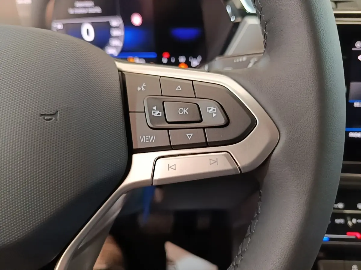 Gros plan sur le volant cuir gris du Volkswagen Touran 2024 avec commandes multifonctions et affichage digital en arrière-plan.