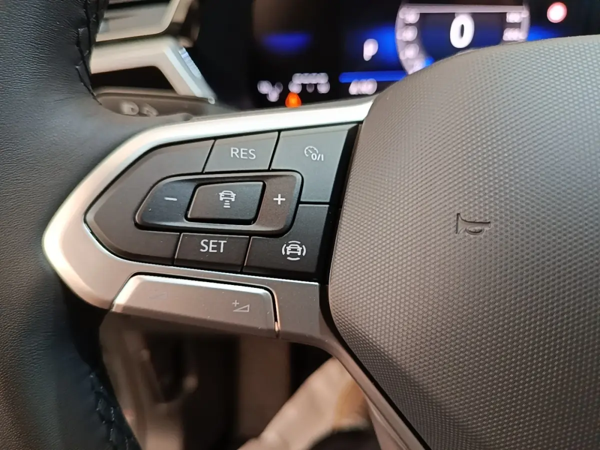 Gros plan sur les commandes à gauche du volant du Volkswagen Touran 2024, boutons noirs et argentés avec affichage numérique flou en arrière-plan.