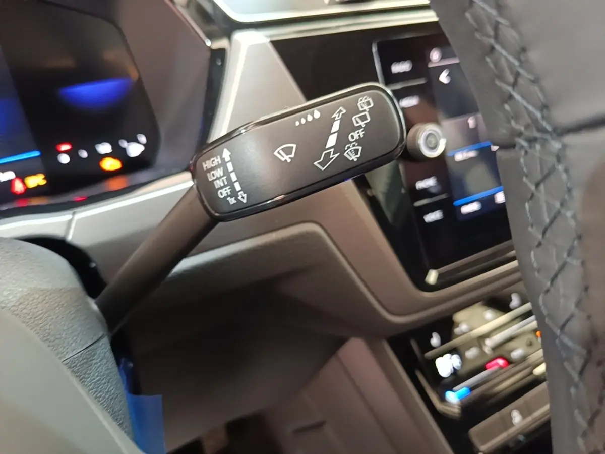 Gros plan sur la commande des essuie-glaces à gauche du volant dans l’habitacle du Volkswagen Touran gris clair 2024.