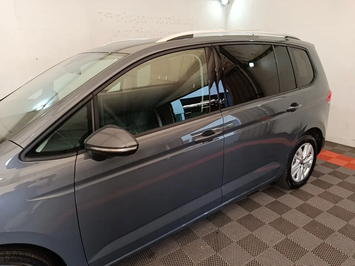 Vue latérale droite d'un Volkswagen Touran gris clair 2024, avec rétroviseur et vitres teintées visibles.