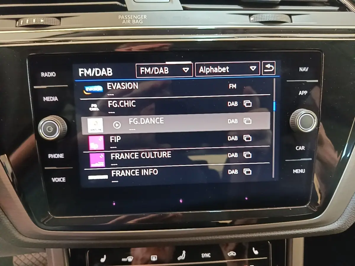 Gros plan sur l'écran tactile central du Volkswagen Touran 2024 affichant les stations radio FM/DAB.