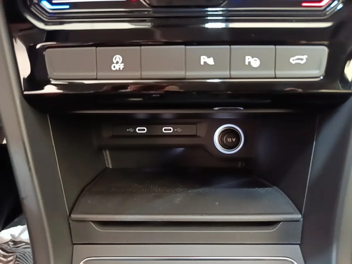 Gros plan sur la console centrale noire du Volkswagen Touran 2024 avec ports USB-C, prise 12V et boutons d’assistance.