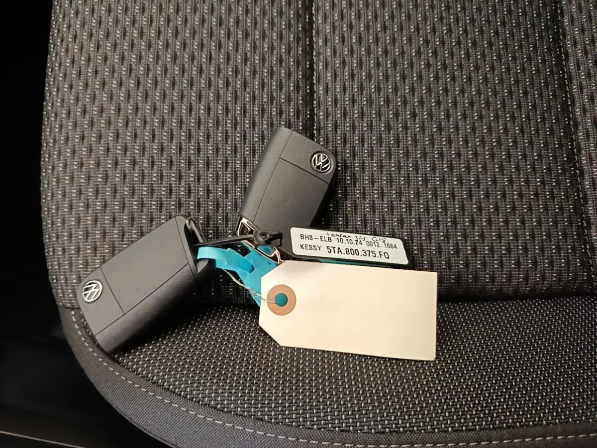 Clés noires Volkswagen posées sur un siège tissu gris foncé, avec une étiquette blanche attachée.