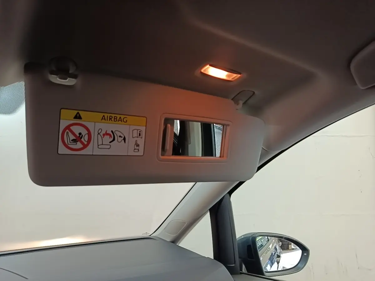 Intérieur du Volkswagen Touran 2024, vue côté passager avec pare-soleil ouvert et rétroviseur extérieur gris clair visible.