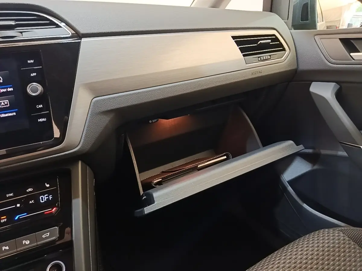 Intérieur Volkswagen Touran 2024 gris clair, vue côté passager avec boîte à gants ouverte et tableau de bord moderne.