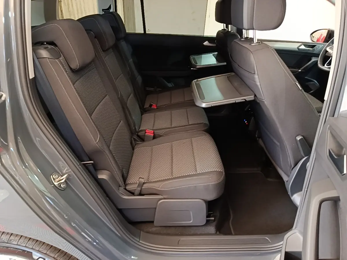 Vue latérale intérieure côté gauche du Volkswagen Touran gris clair 2024, montrant les sièges arrière et une tablette rabattable.