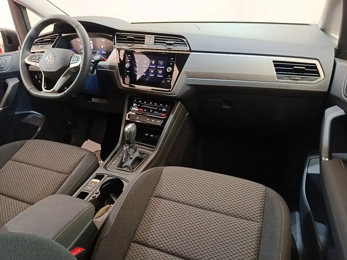 Vue intérieure avant droite du Volkswagen Touran 2024, montrant tableau de bord gris et écran tactile central.