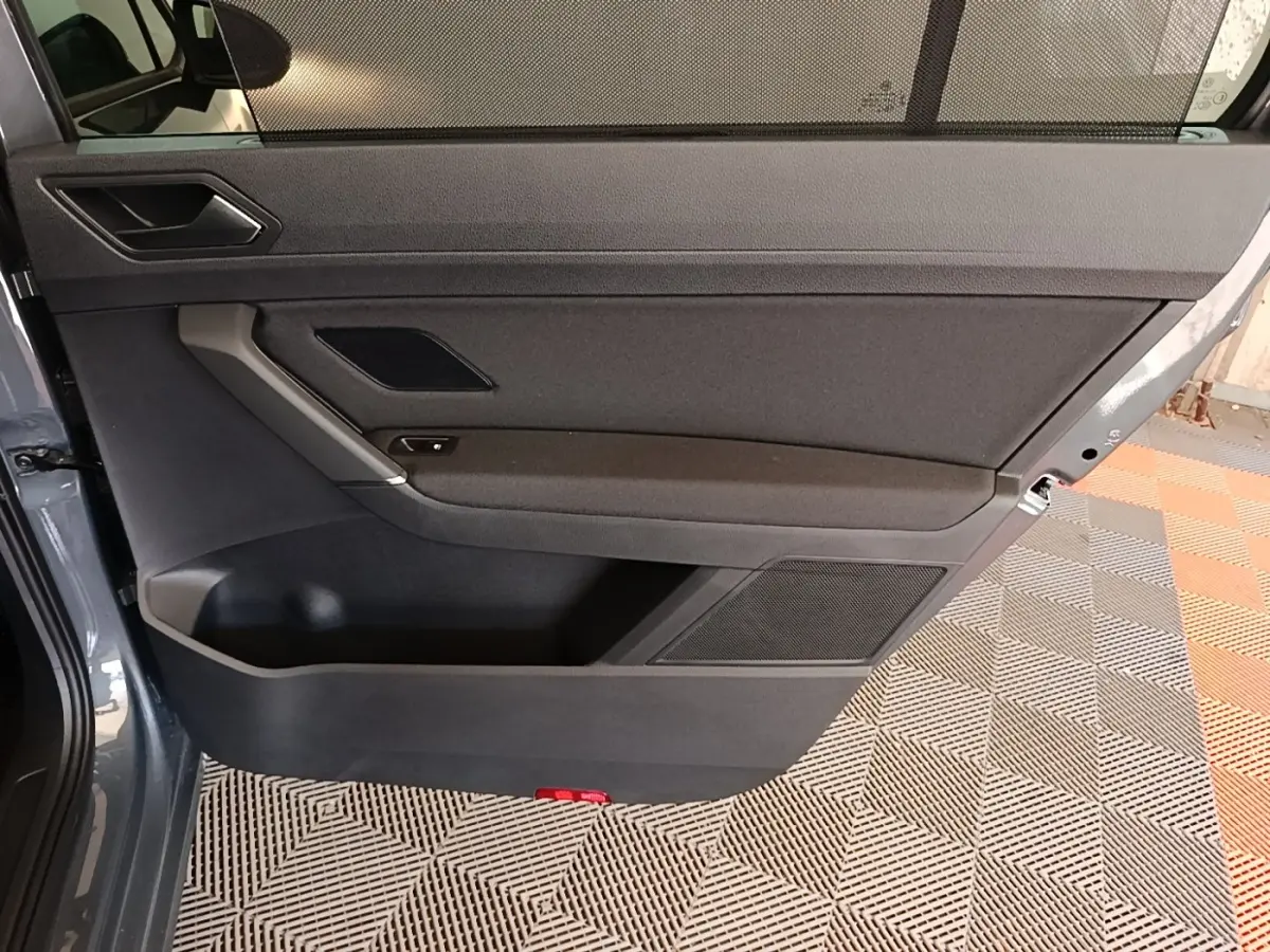 Vue intérieure de la porte avant gauche gris clair du Volkswagen Touran 2024 avec panneau noir et rangement intégré.