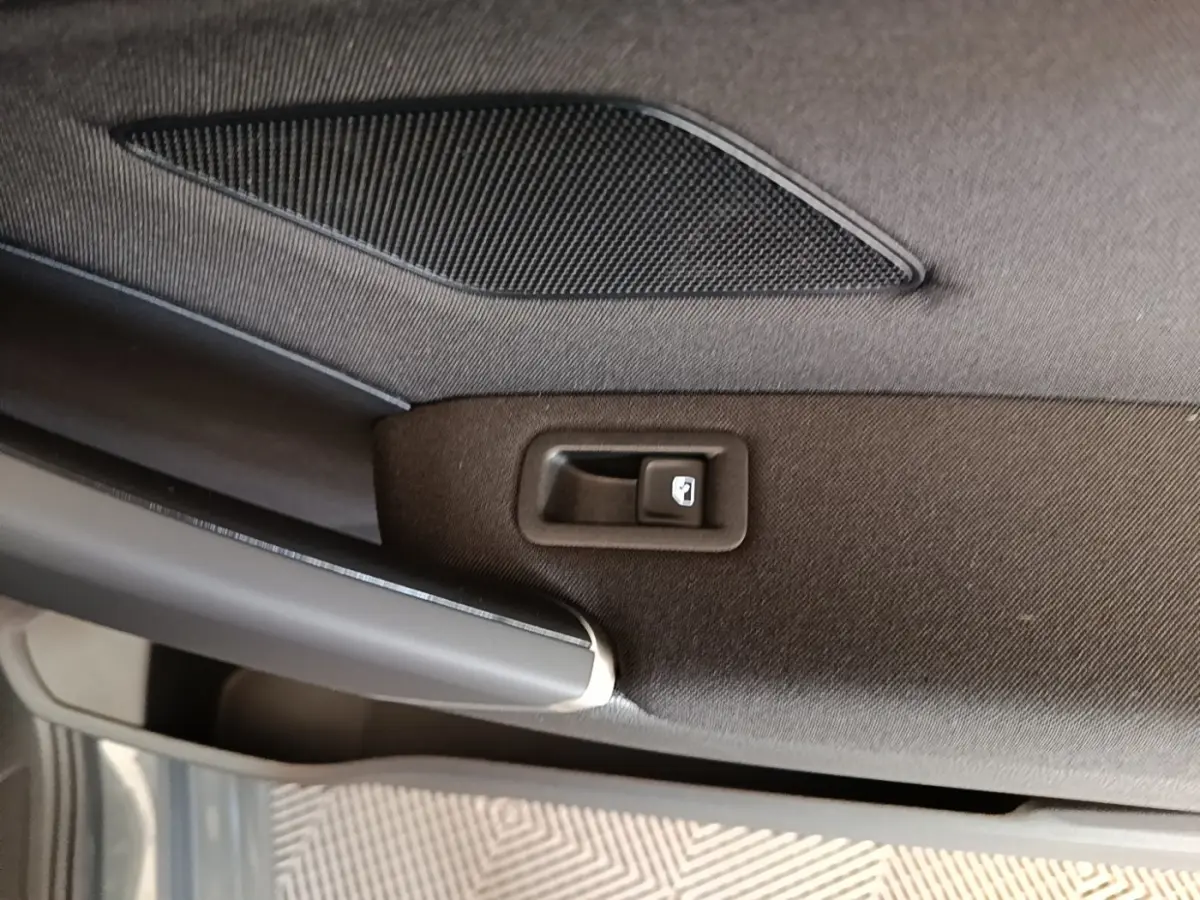 Détail intérieur de la porte arrière droite du Volkswagen Touran gris clair, avec bouton de verrouillage et haut-parleur intégré.