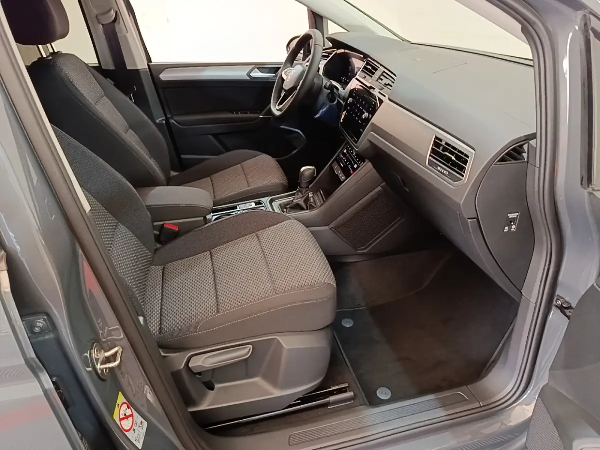 Vue intérieure côté conducteur du Volkswagen Touran gris clair 2024, montrant sièges avant et tableau de bord moderne.
