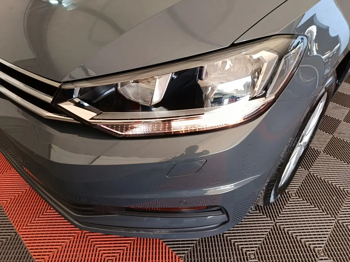 Gros plan sur l'avant droit gris clair du Volkswagen Touran 2024, mettant en valeur le phare LED et la calandre chromée.