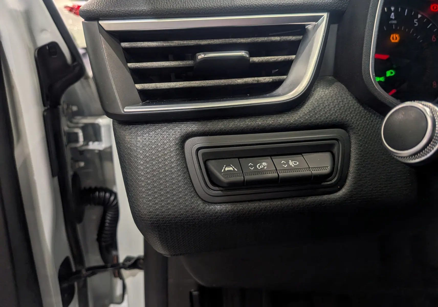 Détail des commandes d'aide à la conduite sur le tableau de bord noir d'une Renault Clio V blanc glacier, côté gauche.