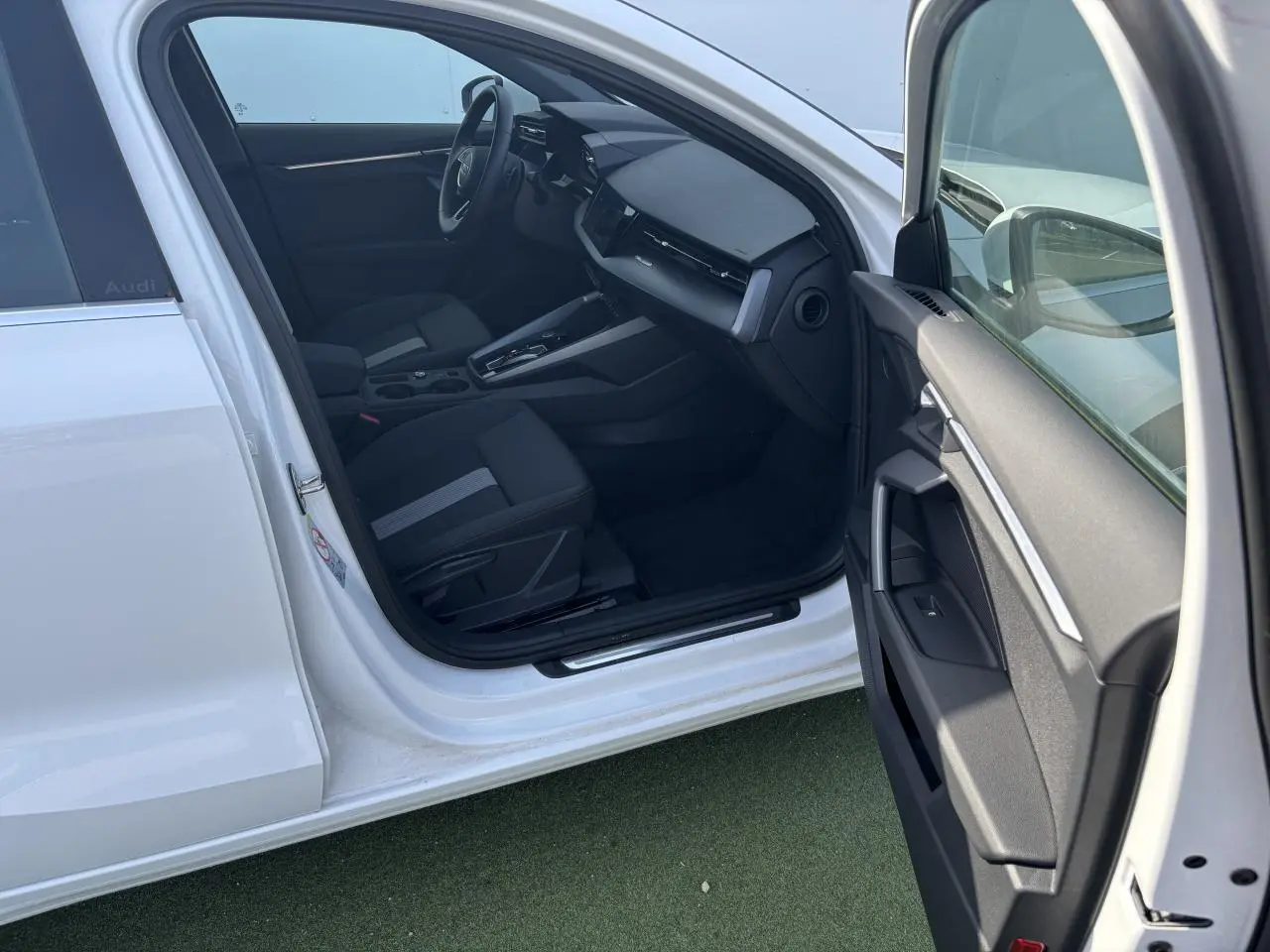 Intérieur côté conducteur d'une Audi A3 Sportback blanche, montrant sièges noirs et tableau de bord moderne.