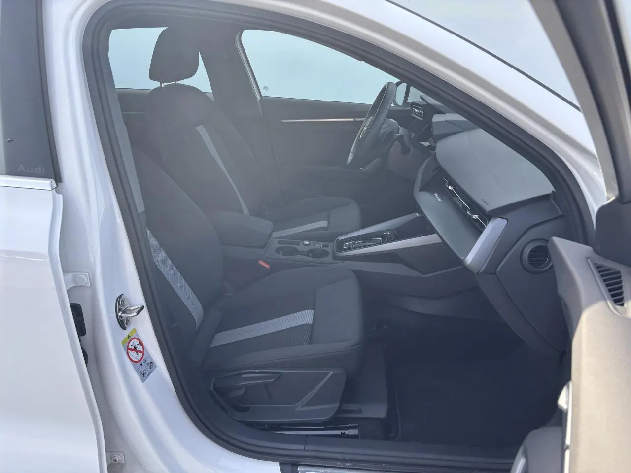 Intérieur avant droit d'une Audi A3 Sportback 2024 blanc Arkona avec sièges tissu noir et console centrale moderne.