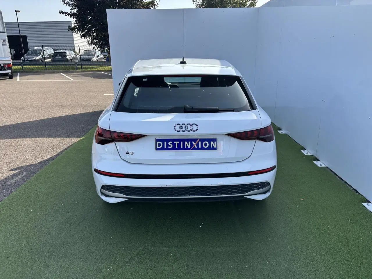 Vue arrière d'une Audi A3 blanche Arkona avec feux arrière LED et logo distinctif sur fond vert.