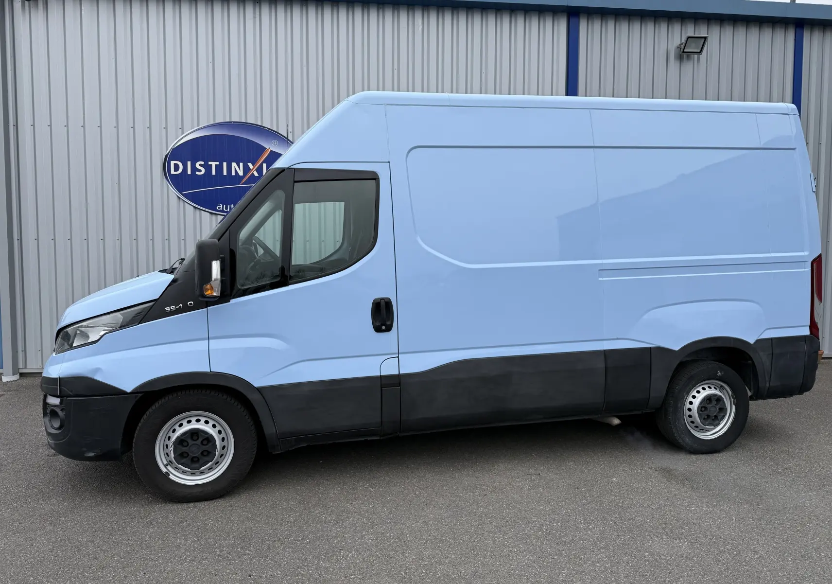 Fourgon Iveco Daily bleu clair en vue profil côté gauche, avec bas de caisse noir et jantes acier simples.