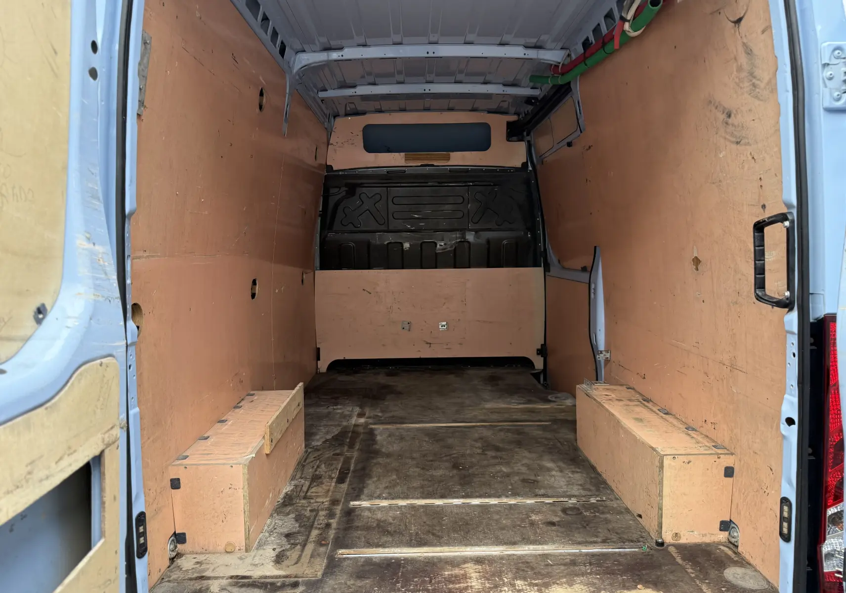 Vue intérieure arrière du fourgon Iveco Daily bleu 2017, montrant l'espace de chargement avec parois en bois et sol usé.