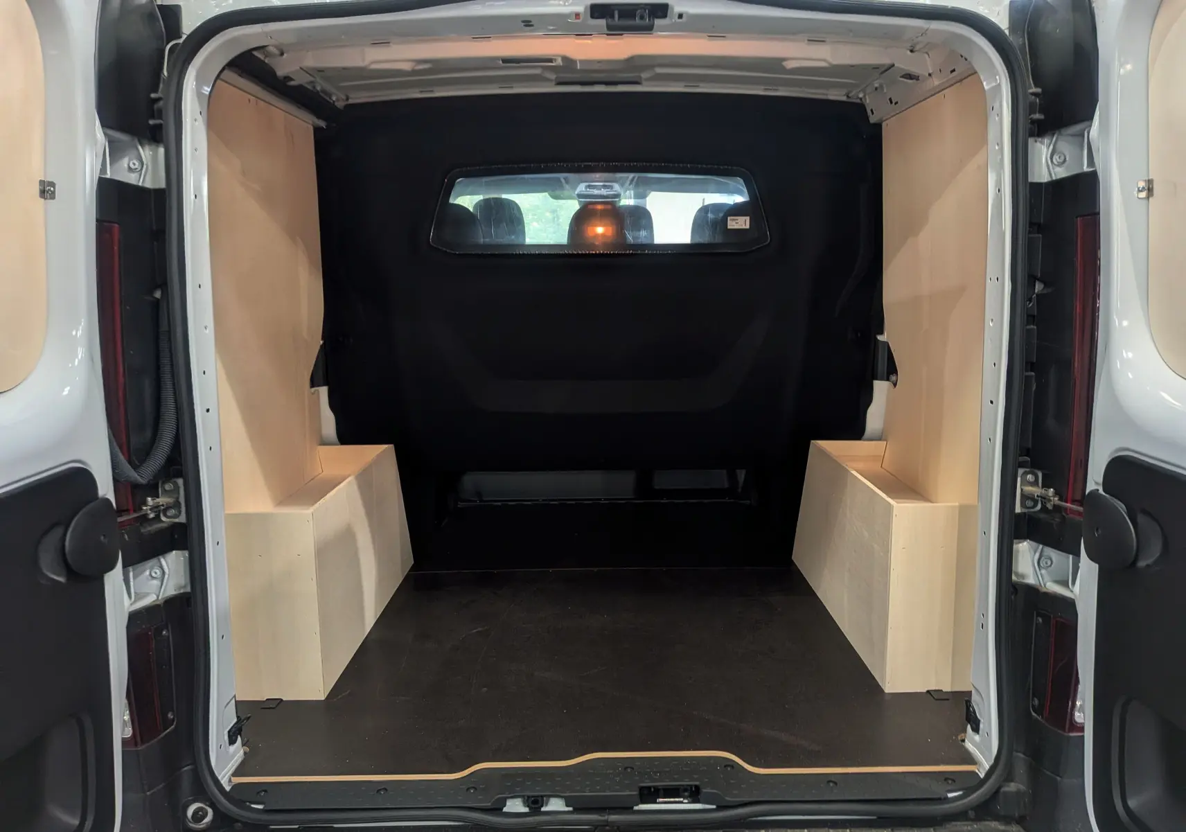 Vue arrière du Renault Trafic cabine approfondie blanc minéral 2023, montrant l'espace de chargement avec habillage bois clair.