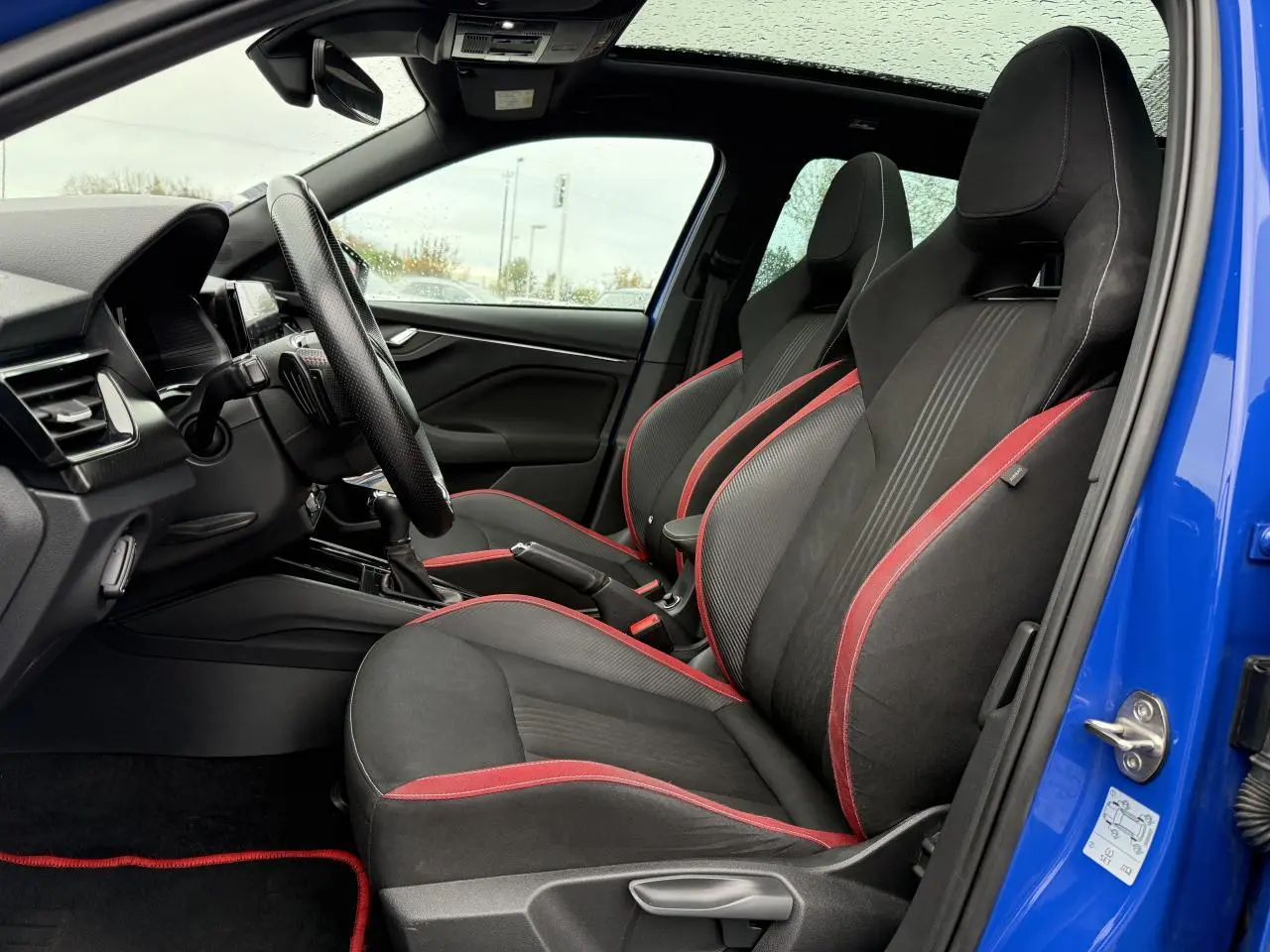 Vue intérieure côté conducteur du Skoda Kamiq bleu Energy 2021, sièges sport noirs avec surpiqûres rouges et volant cuir.