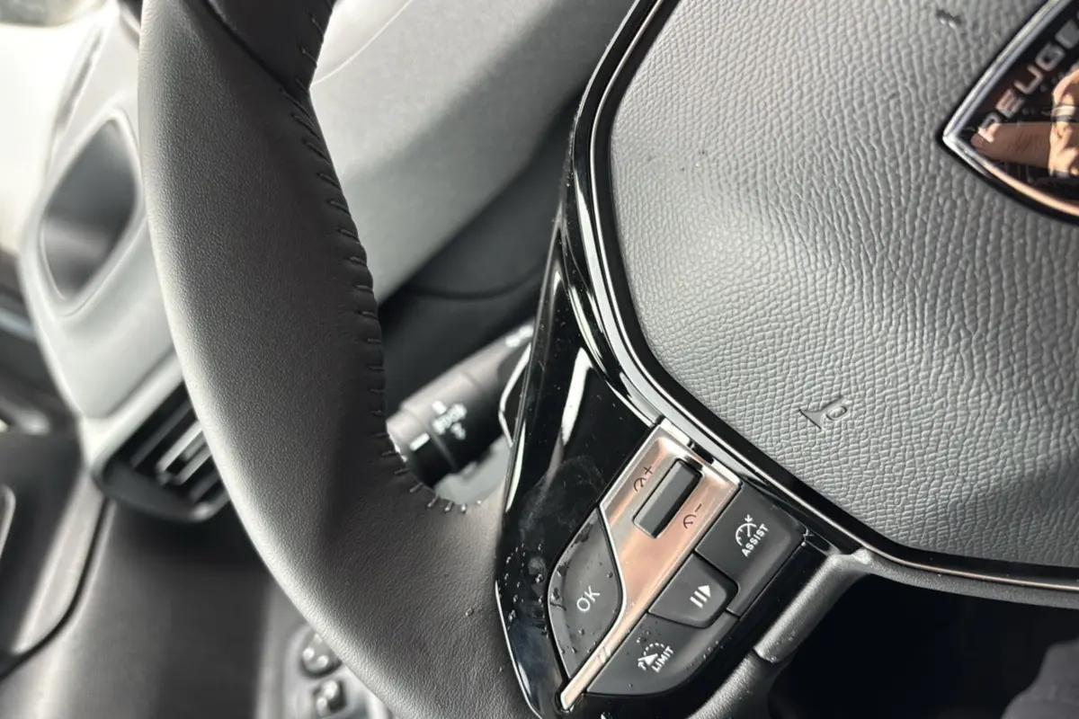 Gros plan sur le volant cuir multifonctions du Peugeot Rifter gris Artense, mettant en valeur les commandes intégrées.