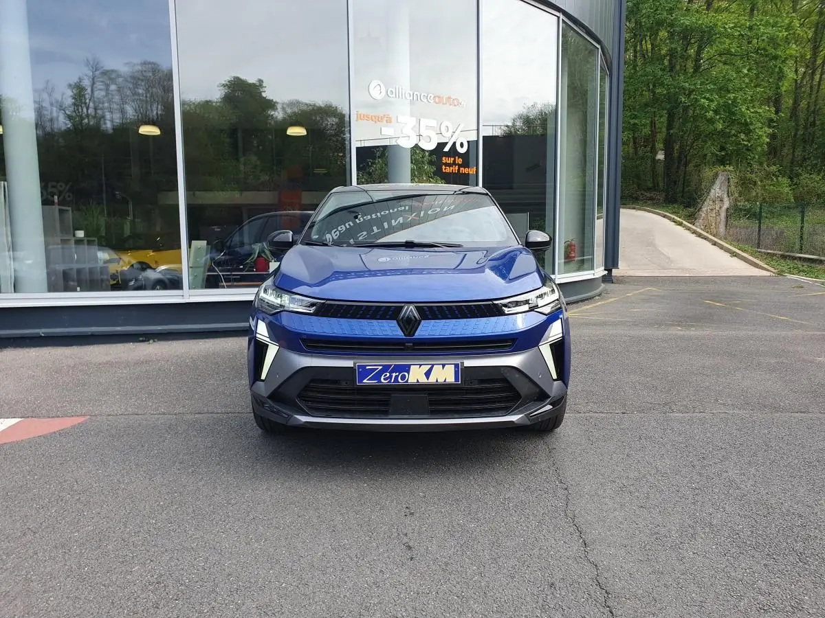 Vue avant d'un Renault Captur bleu Iron 2026 avec calandre moderne et éclairage LED distinctif, stationné devant un showroom.