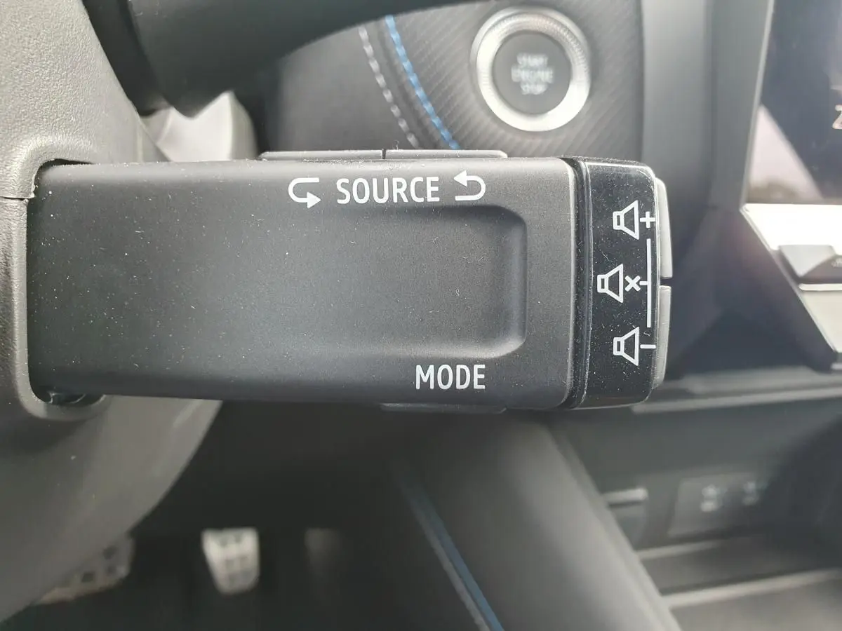 Gros plan sur la commande au volant du Renault Captur 2026, avec bouton source et mode, intérieur noir et surpiqûres bleues.