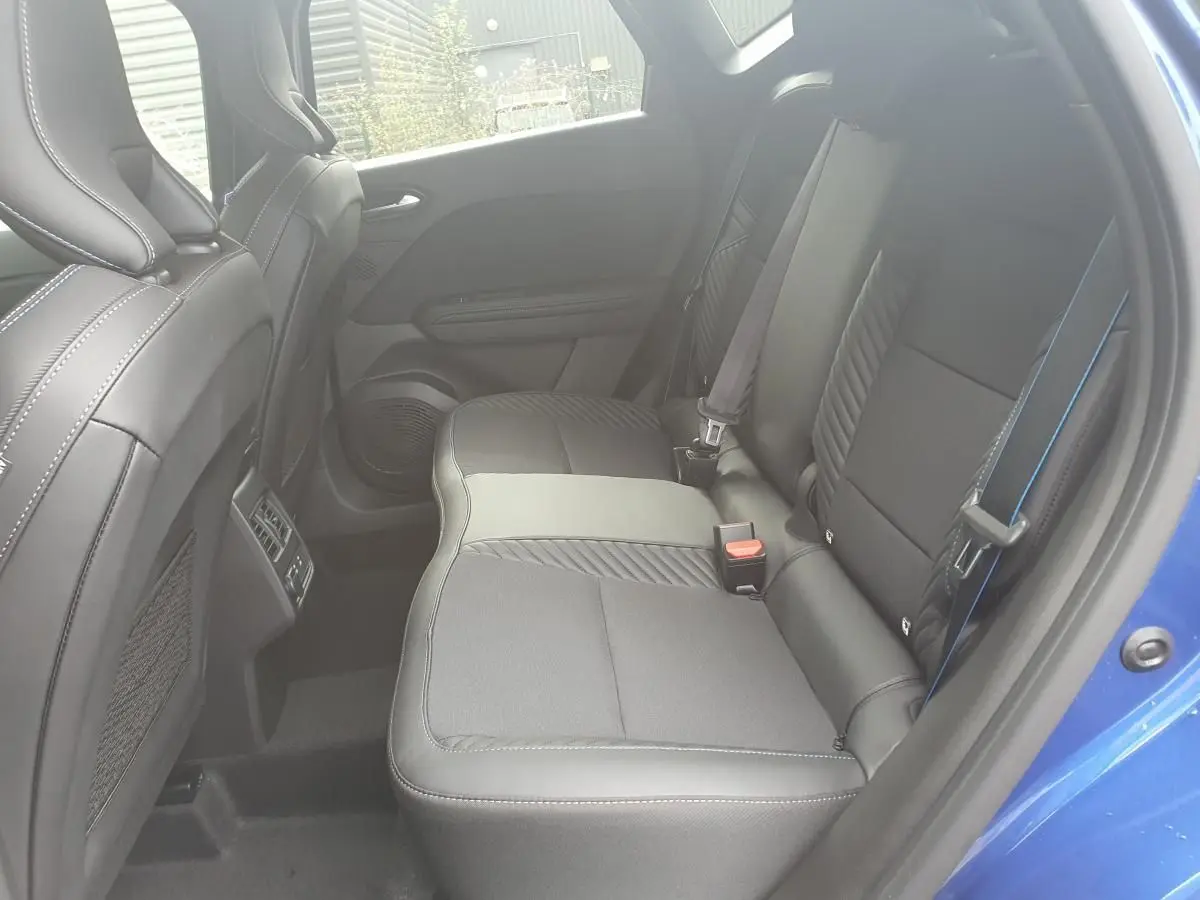 Vue intérieure arrière côté droit du Renault Captur bleu Iron, sièges noirs avec surpiqûres bleues et prises USB visibles.