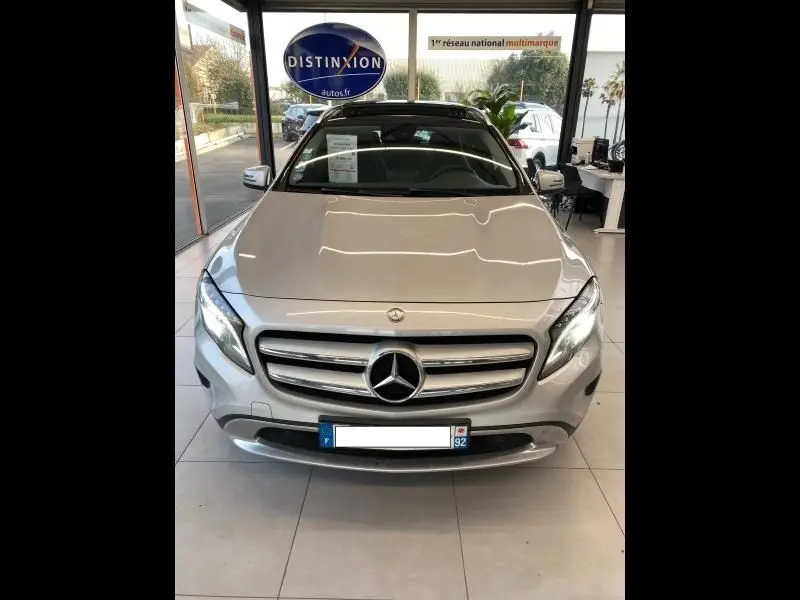 Vue avant d'un Mercedes GLA 200 Sensation gris montagne, avec calandre chromée et phares LED allumés en showroom.