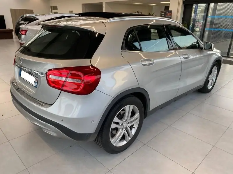 Vue 3/4 arrière droite d'un Mercedes GLA 200 Sensation gris montagne avec toit panoramique et jantes alliage en showroom.