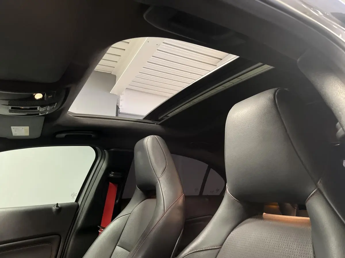 Intérieur de la Mercedes Classe A 45 AMG 2015, vue des sièges sport noirs avec surpiqûres rouges et toit ouvrant panoramique.