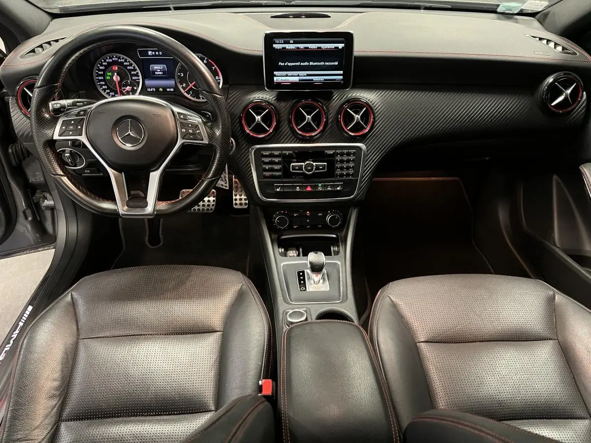 Intérieur de Mercedes Classe A 45 AMG 2015, vue avant centrée sur tableau de bord en carbone et sièges cuir noirs.