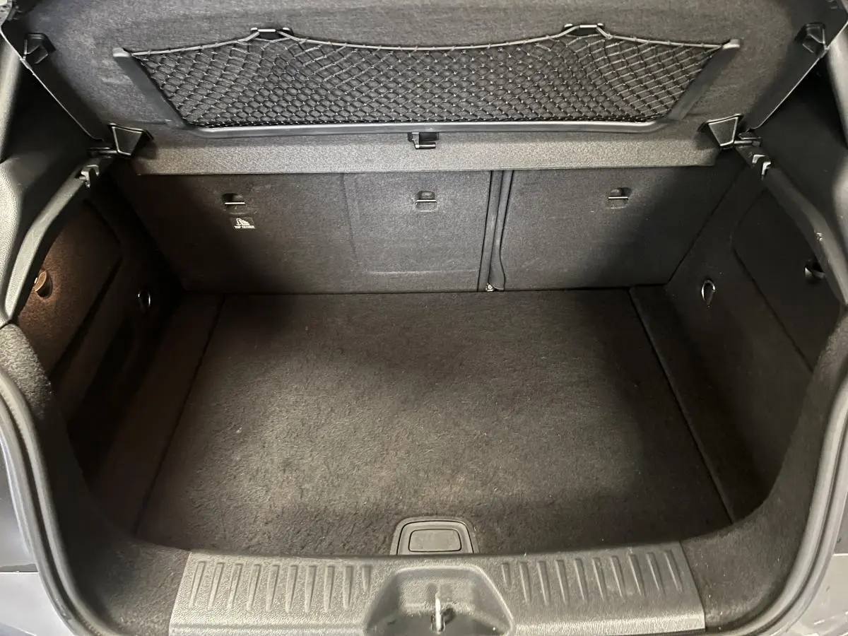 Coffre ouvert de la Mercedes Classe A 45 AMG gris, vue intérieure montrant le tapis et filet de rangement au dos du hayon.