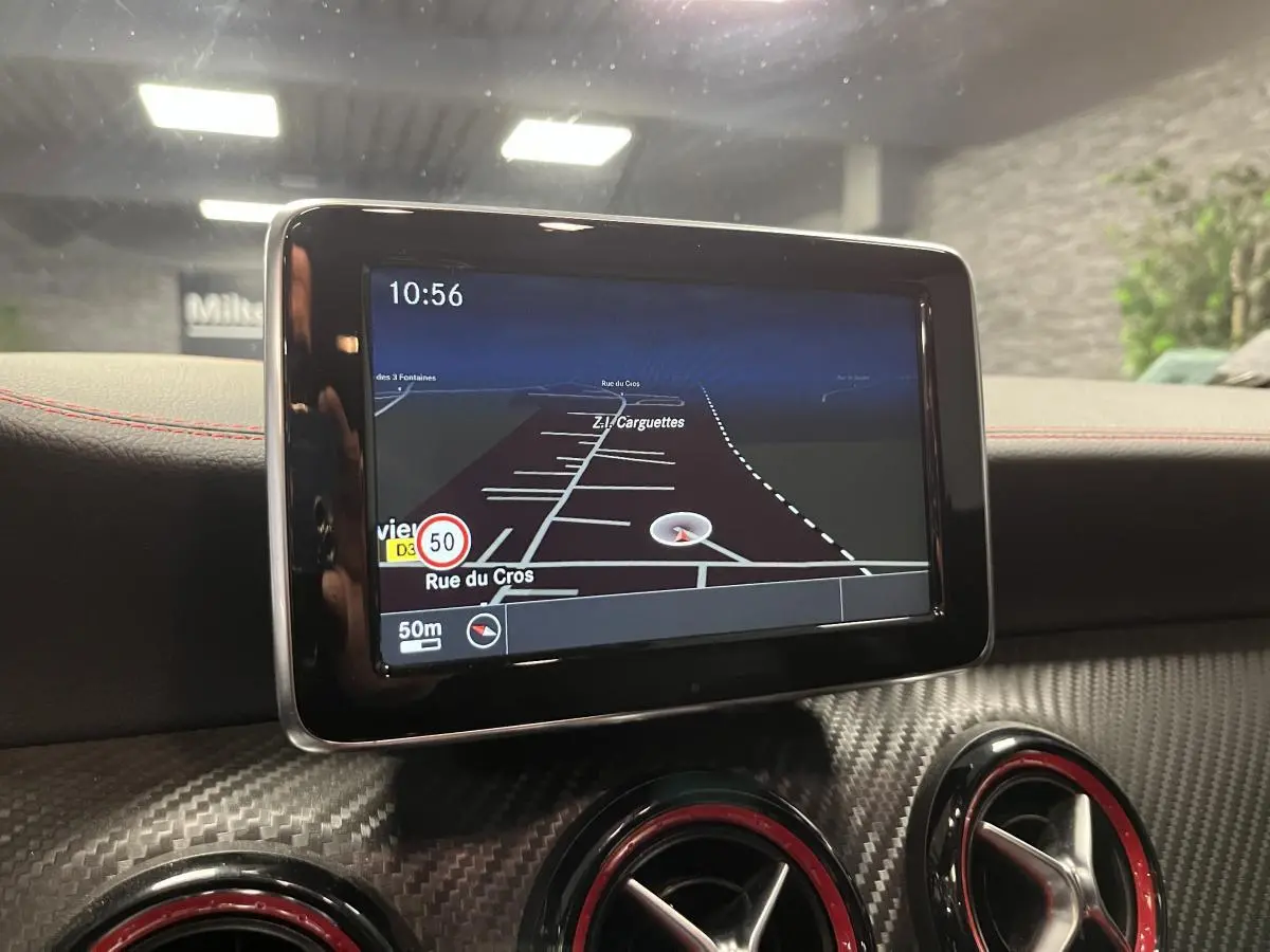 Écran GPS central avec carte, entouré de buses d'aération rouges sur tableau de bord carbone d'une Mercedes Classe A grise.