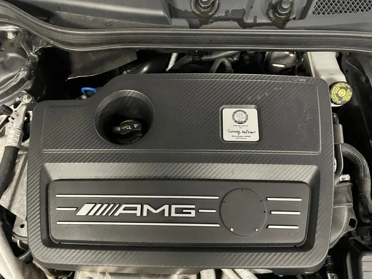 Vue plongeante sur le moteur AMG noir texturé de la Mercedes Classe A 45 AMG 2015 avec plaque constructeur visible.
