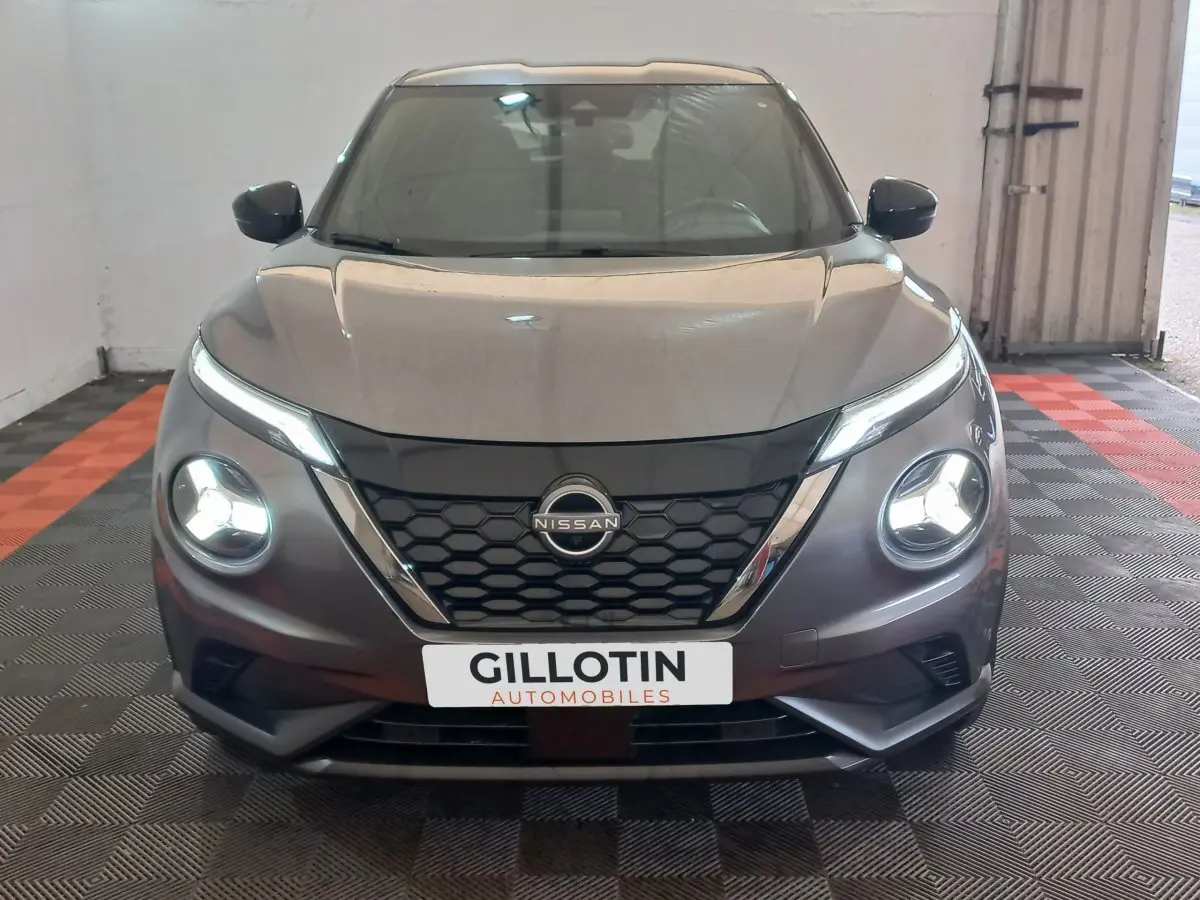 Vue avant d'un Nissan Juke Hybrid gris foncé avec phares LED allumés, calandre noire et logo central visible.