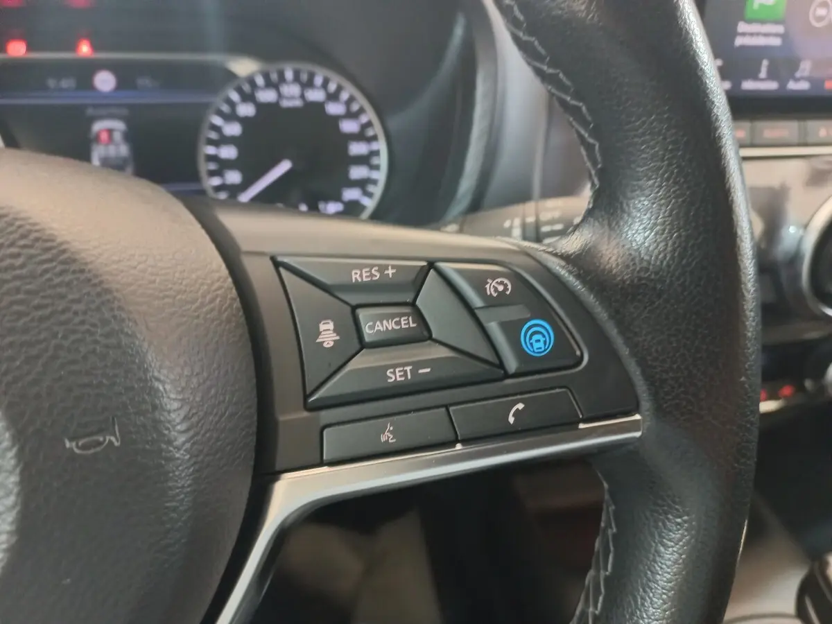 Gros plan sur le volant cuir et alu côté gauche du Nissan Juke Hybrid 143 Business+ 2023 avec commandes multifonctions.