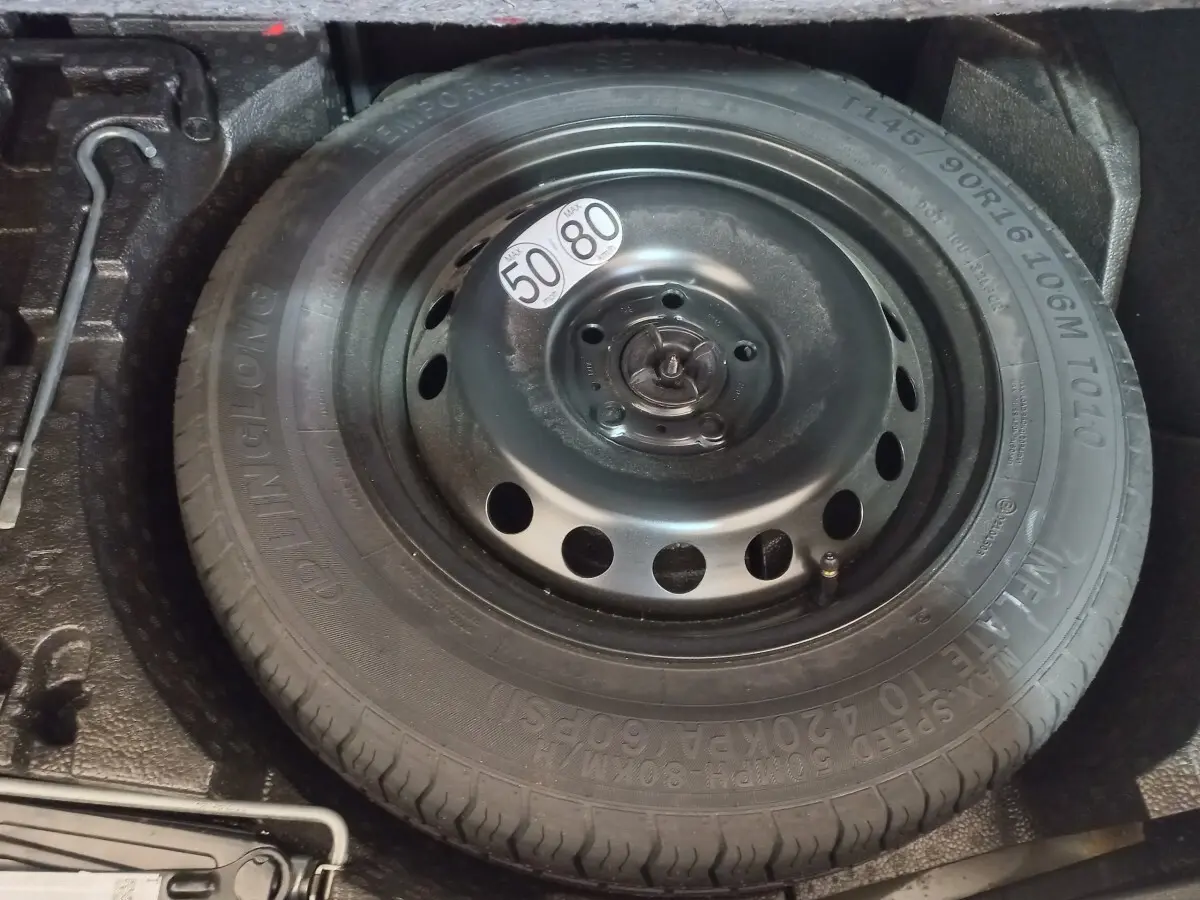Gros plan sur la roue de secours noire dans le coffre du Nissan Juke Hybrid 143 Business+ gris foncé.