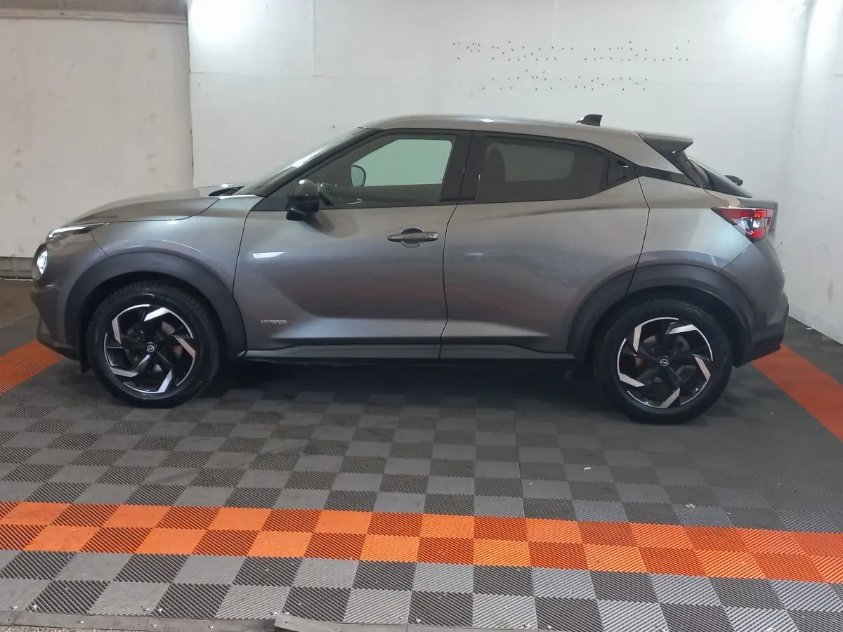 Vue de profil côté gauche du Nissan Juke Hybrid 143 Business+ gris foncé avec jantes noires et détails noirs contrastants.
