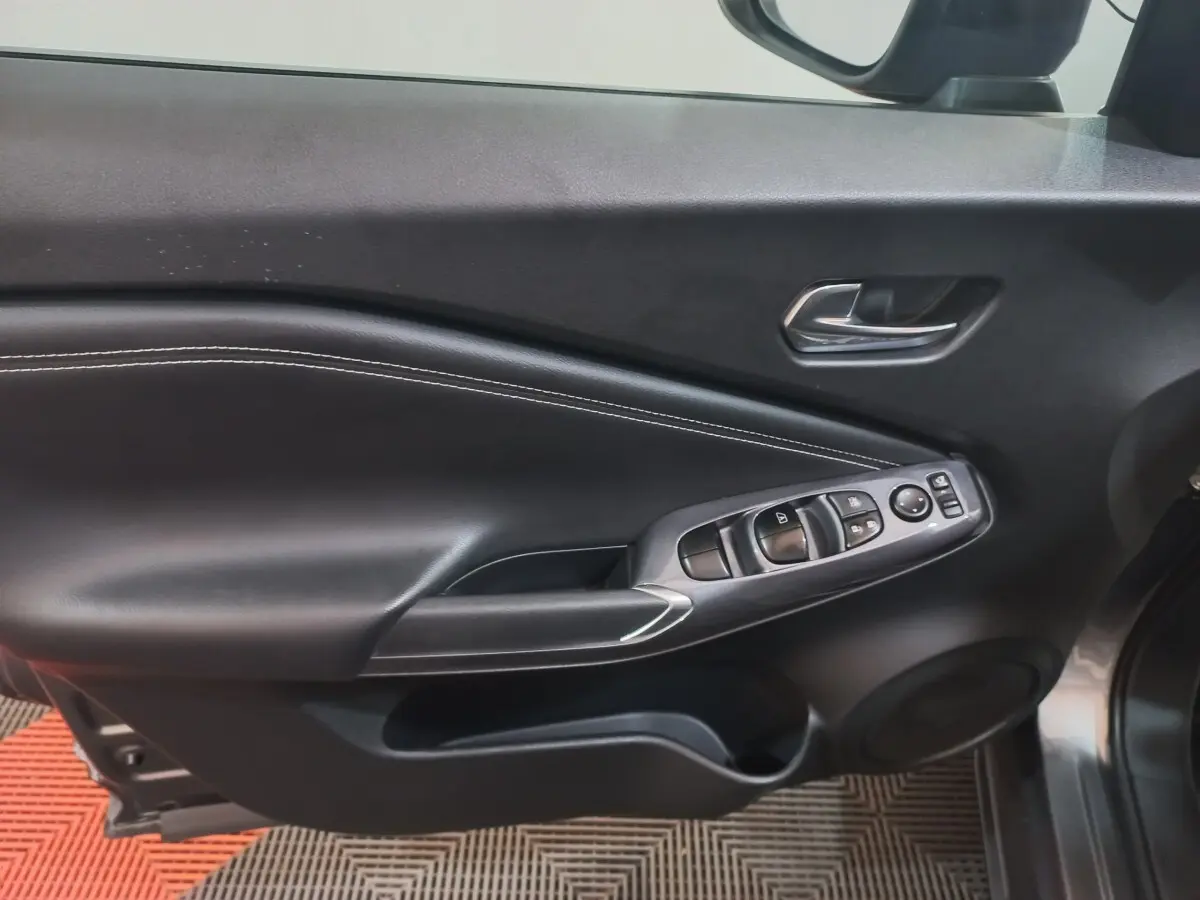 Vue intérieure du panneau de porte côté conducteur du Nissan Juke Hybrid 143 Business+ gris foncé, avec commandes électriques et surpiqûres blanches.