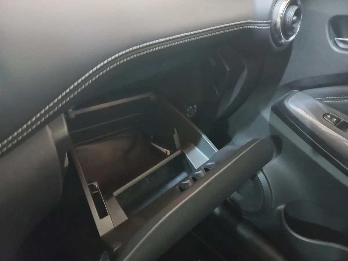 Intérieur du Nissan Juke Hybrid 2023, vue sur la boîte à gants ouverte avec surpiqûres blanches sur tableau de bord noir.