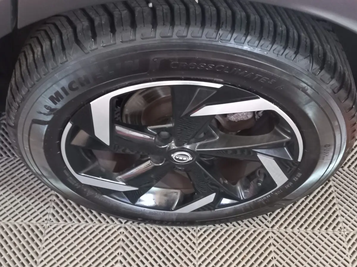 Gros plan sur la jante noire et argentée du Nissan Juke Hybrid 143 Business+ gris foncé, avec pneu Michelin CrossClimate.