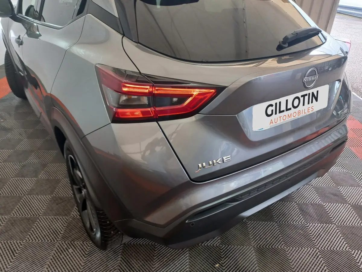 Vue 3/4 arrière droite du Nissan Juke Hybrid gris foncé avec feux LED allumés et logo visible sur hayon.