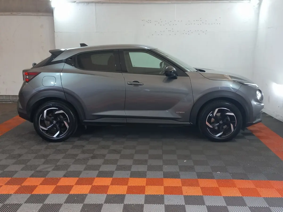Vue profil droit du Nissan Juke Hybrid 143 Business+ gris foncé avec jantes noires et détails hybrides visibles.