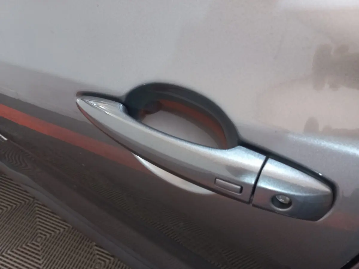 Poignée de porte côté gauche gris foncé du Nissan Juke Hybrid 143 Business+ 2023, avec bouton de déverrouillage intégré.